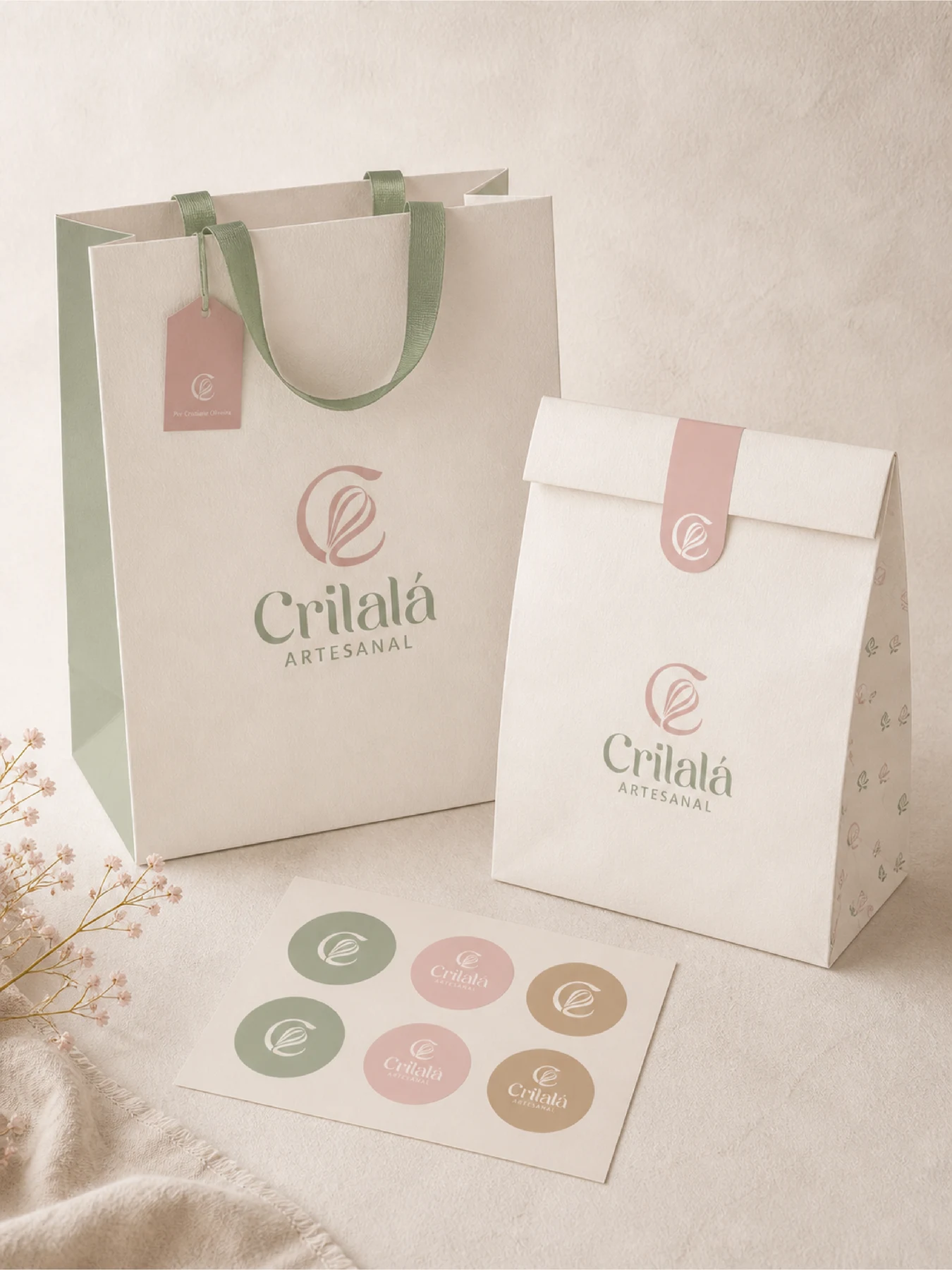 Sacolas e adesivos Crilalá Artesanal com símbolo e assinatura em tons suaves.