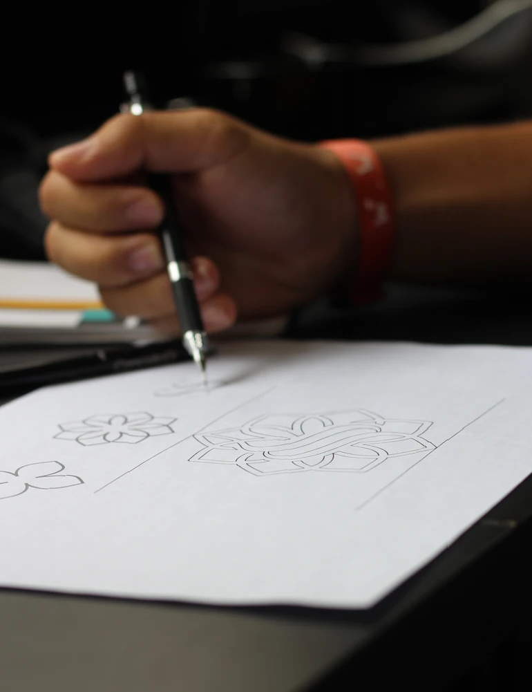 Detalhe da mão de Rafael desenhando alternativas de um símbolo no papel.
